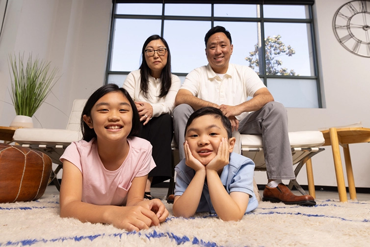 A smiling family with a boy and girl lying on the floor and parents sitting behind them.